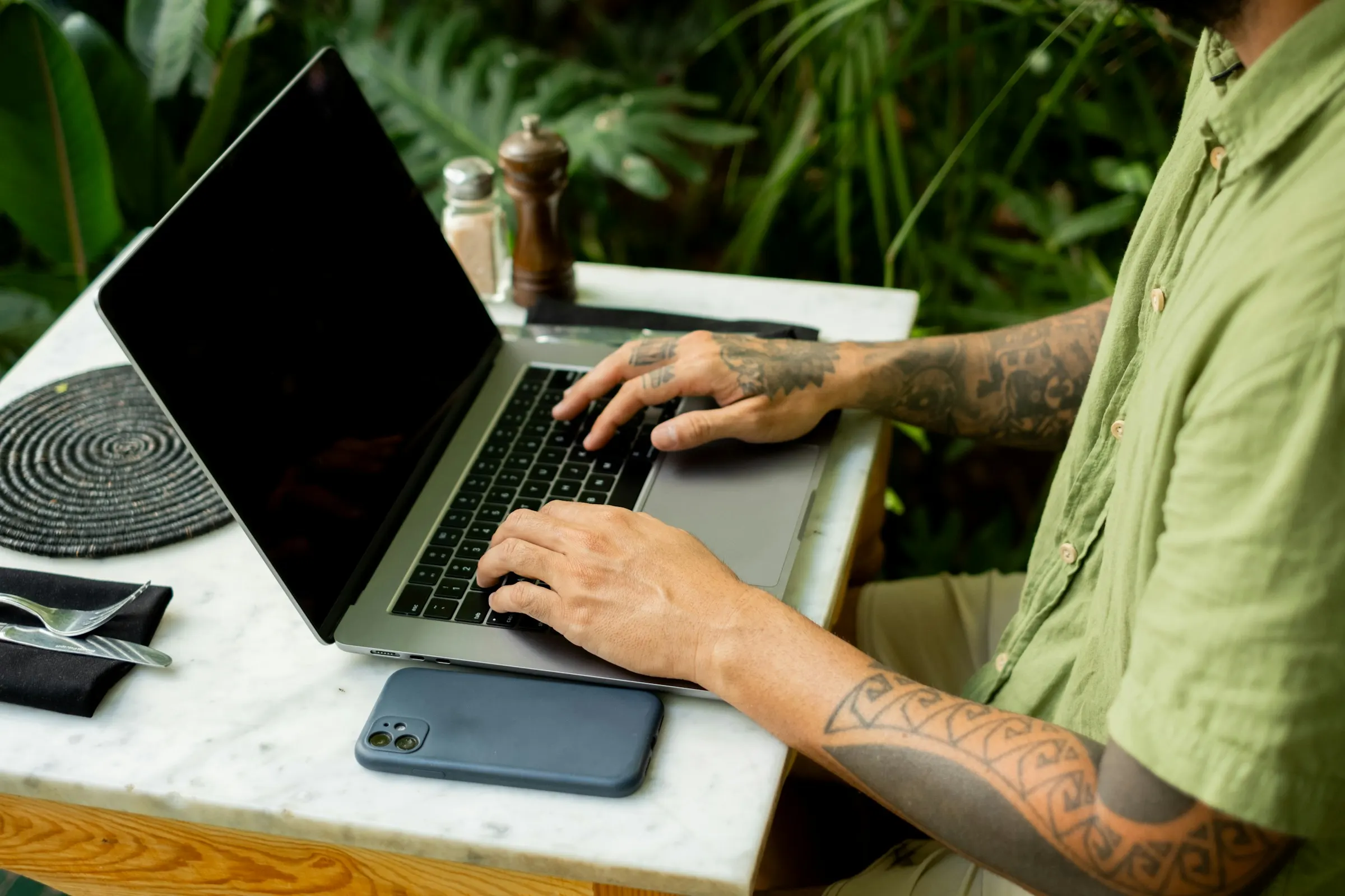 Hands typing on a laptop at a café table, with plants behind